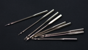 A bunch of sewing machine needles laying on a black fabric